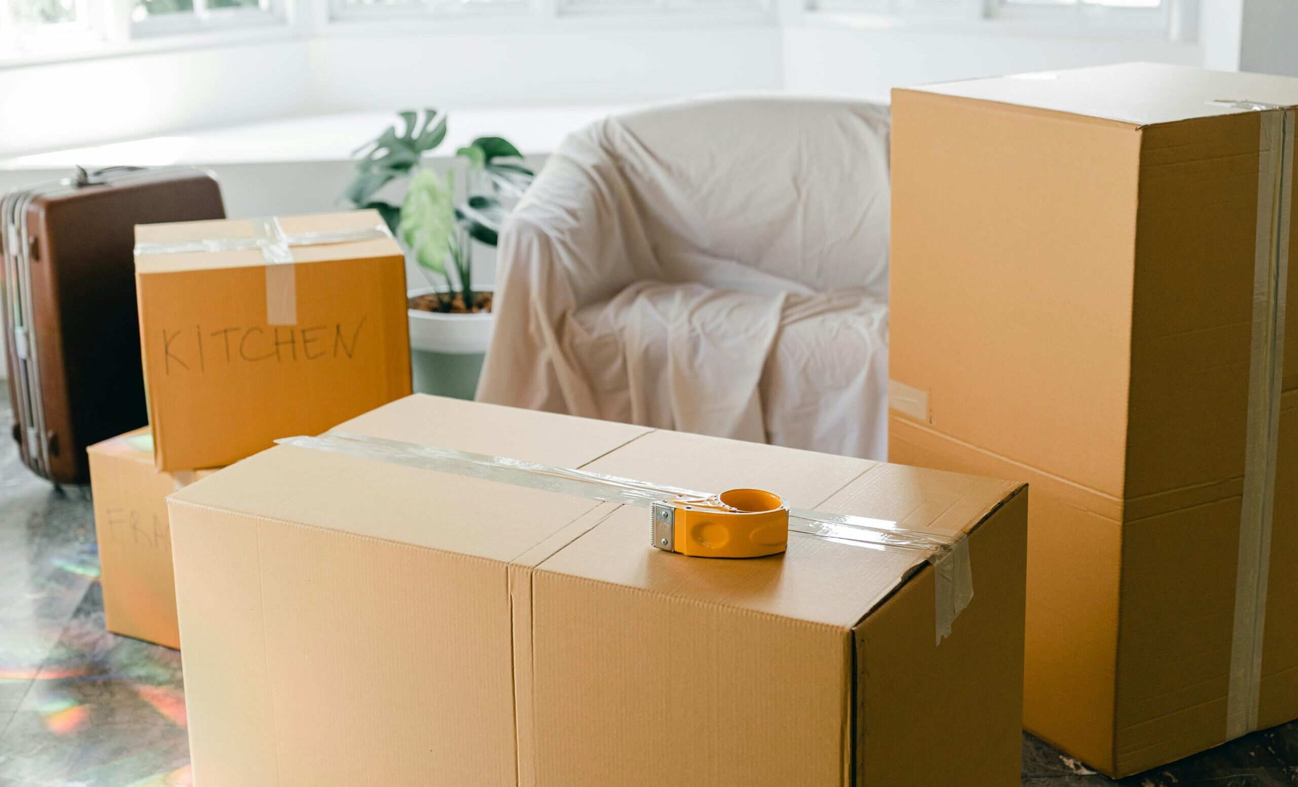 Cardboard boxes labeled 'Kitchen' in sunlit living room, ready for relocation.
