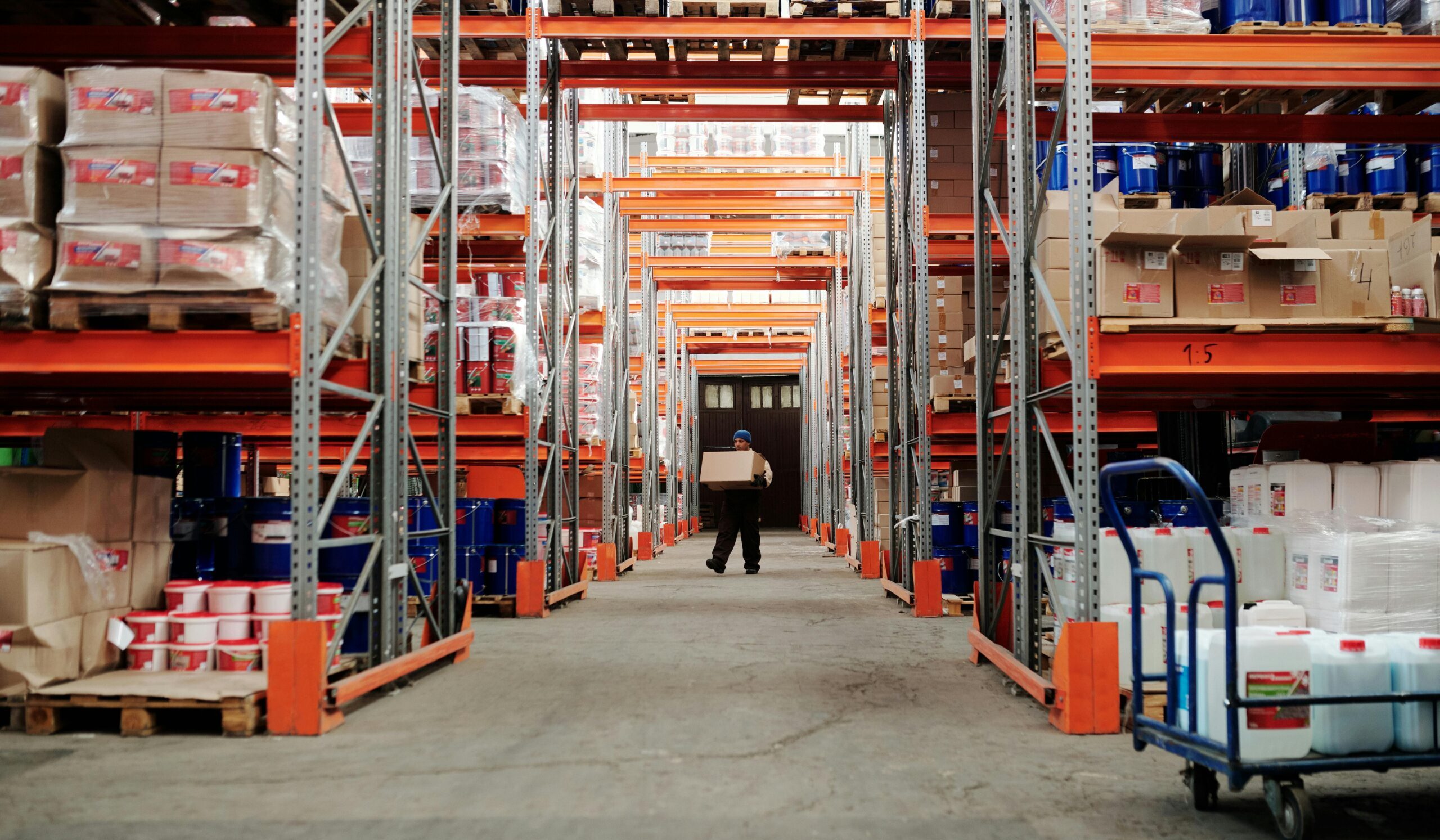 A worker carrying a box in a well-organized warehouse storage aisle.